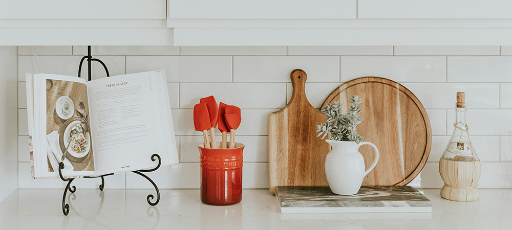 A classic white kitchen with a subway tile backsplash, featuring a cookbook, spatulas, a cutting board, and a vase of flowers