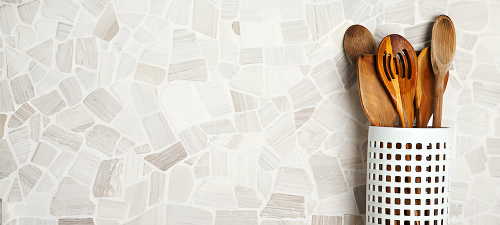 Textured white ceramic mosaic backsplash with irregular pattern shown with wooden utensils in decorative holder