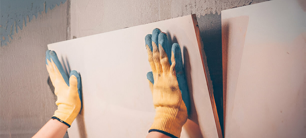 Close-up of gloved hands installing a large format tile backsplash