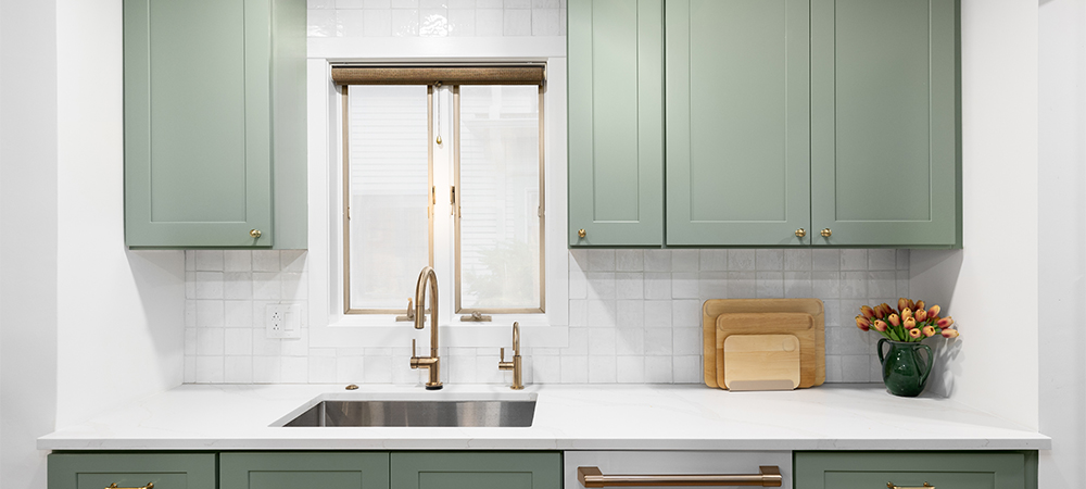 A kitchen with green cabinets, a white subway tile backsplash, and a farmhouse sink.