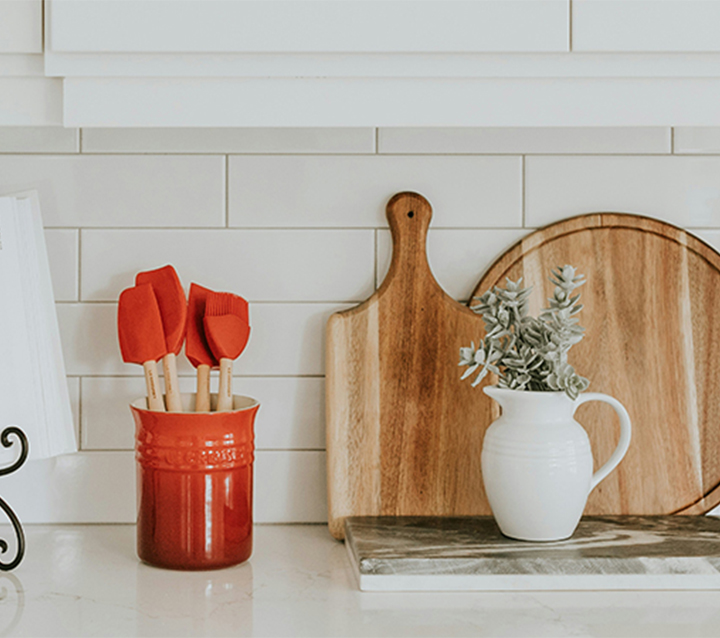 A classic white kitchen with a subway tile backsplash, featuring a cookbook, spatulas, a cutting board, and a vase of flowers