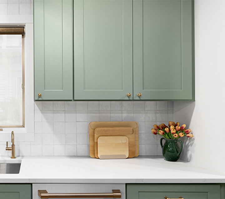 A kitchen with green cabinets, a white subway tile backsplash, and a farmhouse sink.