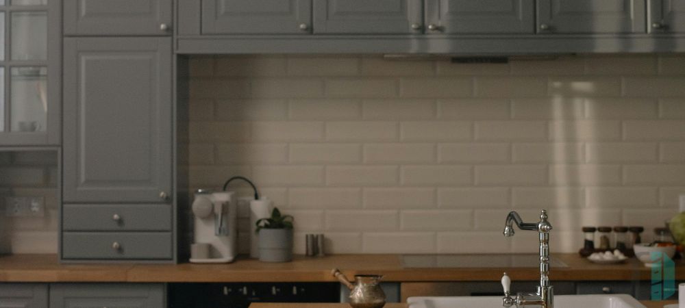 A kitchen with gray shaker cabinets and a natural stone backsplash featuring a mix of white and gray tones